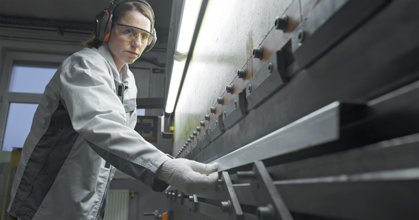 Women wearing protective goggles, gloves, and ear muffs, operating a press brake